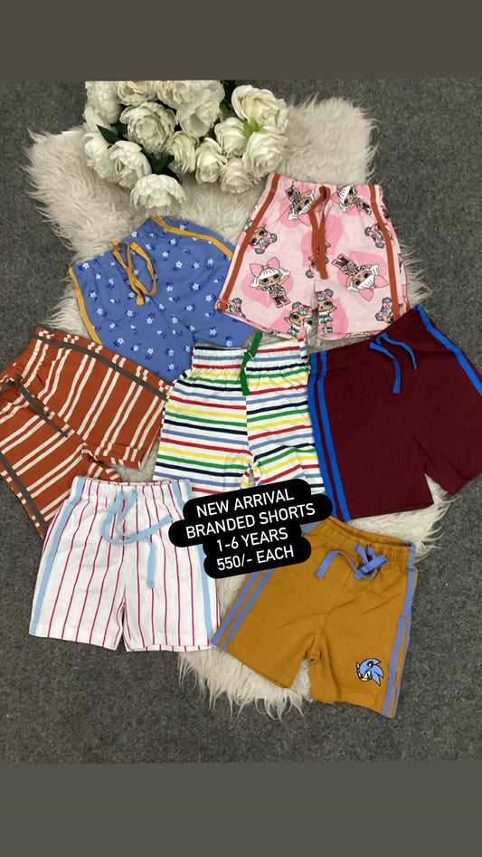 Collection of colorful children's shorts on a textured surface with flowers in the background.