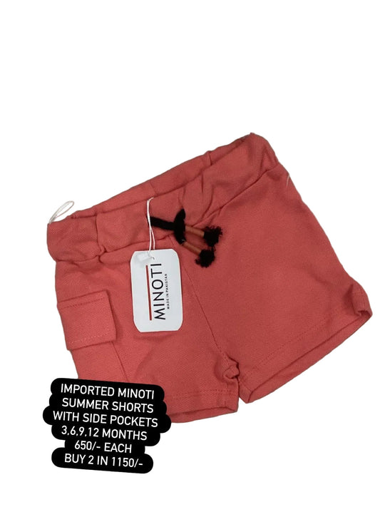 Red shorts with a Minoti tag on a textured surface with flowers in the background