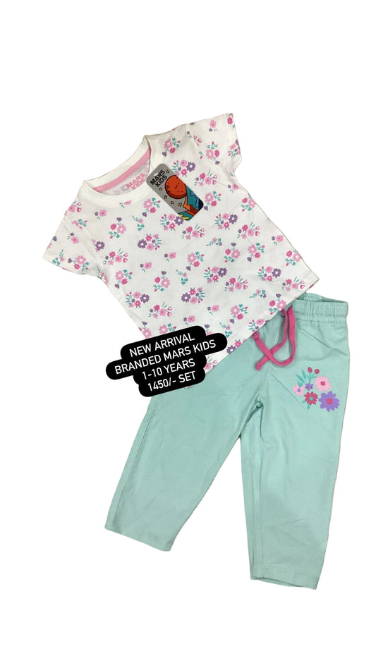 Children's outfit with floral top and light blue pants on a textured surface with flowers.